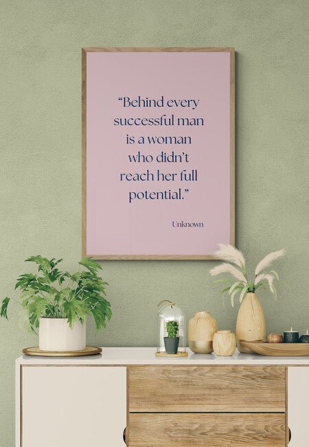 Framed motivational quote on a wall "behind every successful man is a woman who didn't reach her full potential" above a wooden cabinet with decor items.