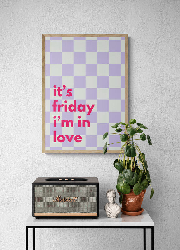Framed checkered poster with 'it's friday i'm in love' text, Marshall speaker, plant, and bust on a table against a gray wall.