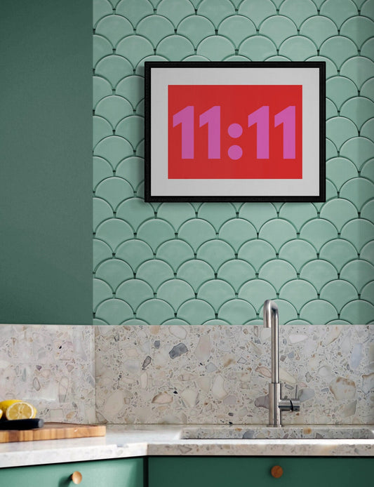 Art poster in red and pink displaying '11:11' angel time on a green tiled wall above a kitchen counter.