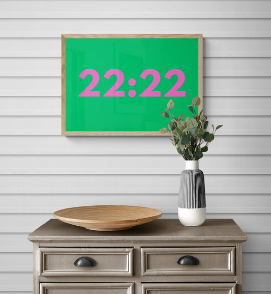Green frame with angel time '22:22' on a wall above a wooden dresser with decor items in bright green and pink.