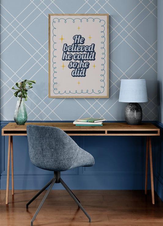 Home office with wooden desk, gray chair, and motivational poster on blue wall with the words he believed he could so he did. 
