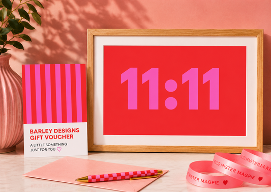 Framed artwork with '11:11' on a red background, gift voucher, pen, and ribbons on a wooden surface.