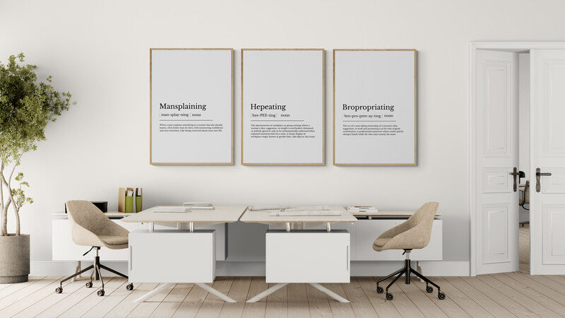 Modern office setup with a desk, chairs, and motivational definition posters on a white wall with mansplaining, hepeating, bropropriating for international women's day.