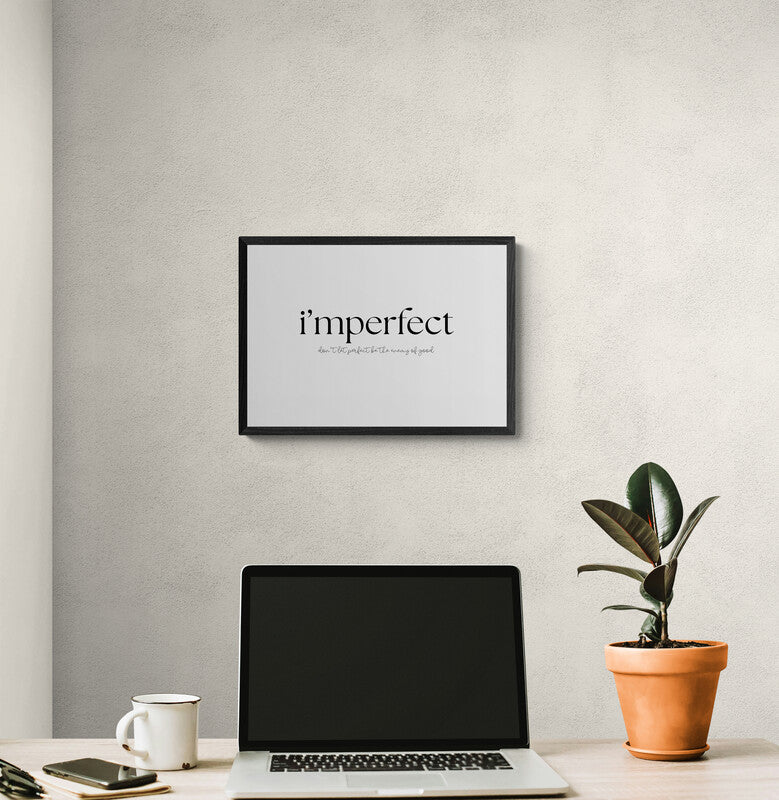 Print with 'imperfect' on a wall in bold typographic print and the wording don't let perfect be the enemy of good underneath, framed above a laptop and plant.