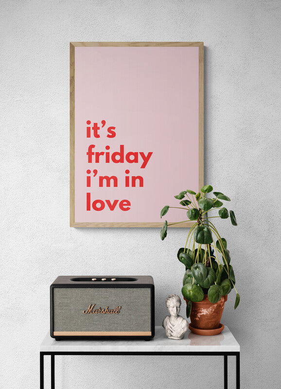 Framed poster with 'it's friday i'm in love' text, Marshall speaker, plant, and bust on a table against a gray wall.