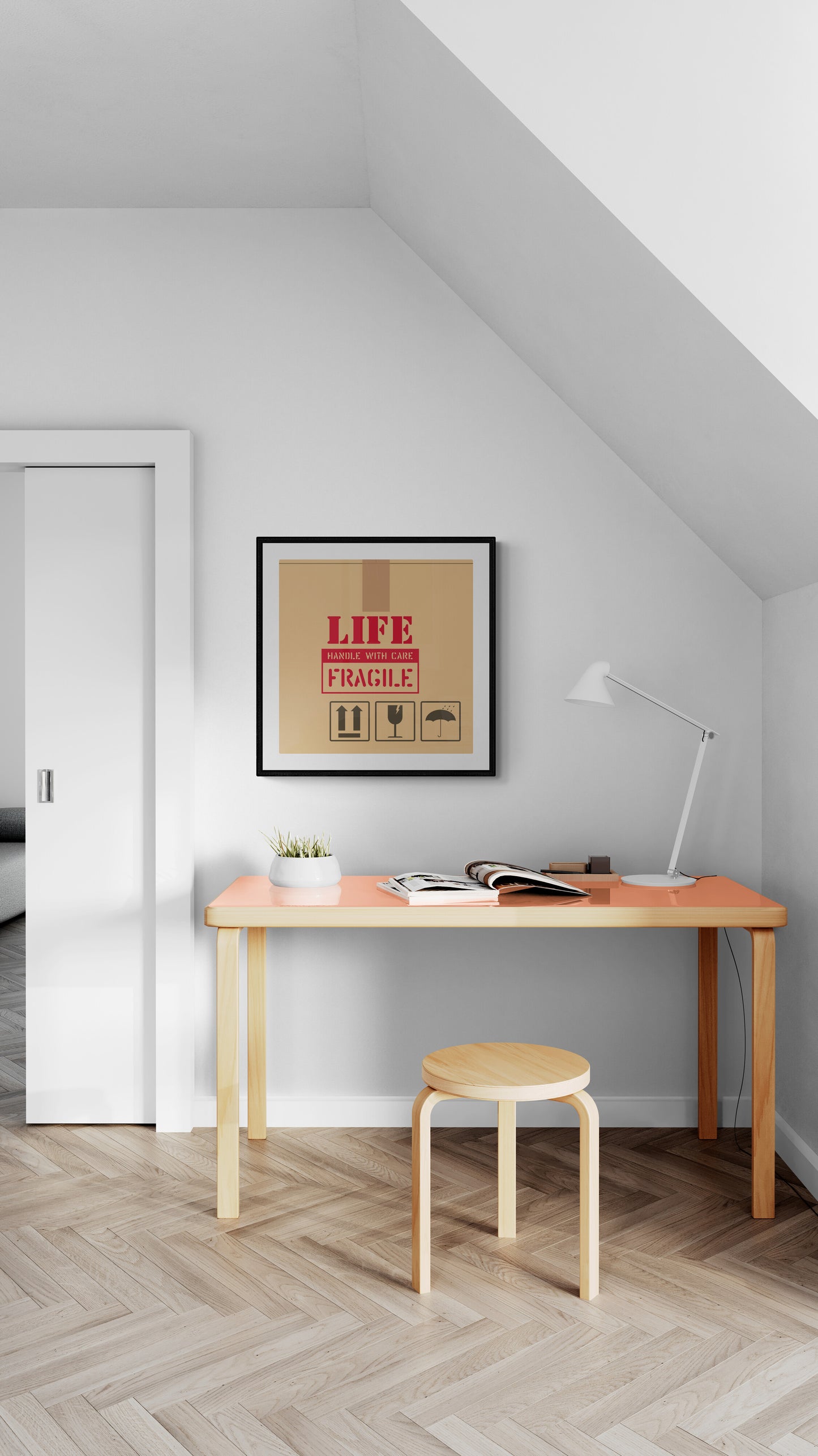 A framed art print with the text 'LIFE IS FRAGILE' displayed on a wall above a desk with a chair and lamp.