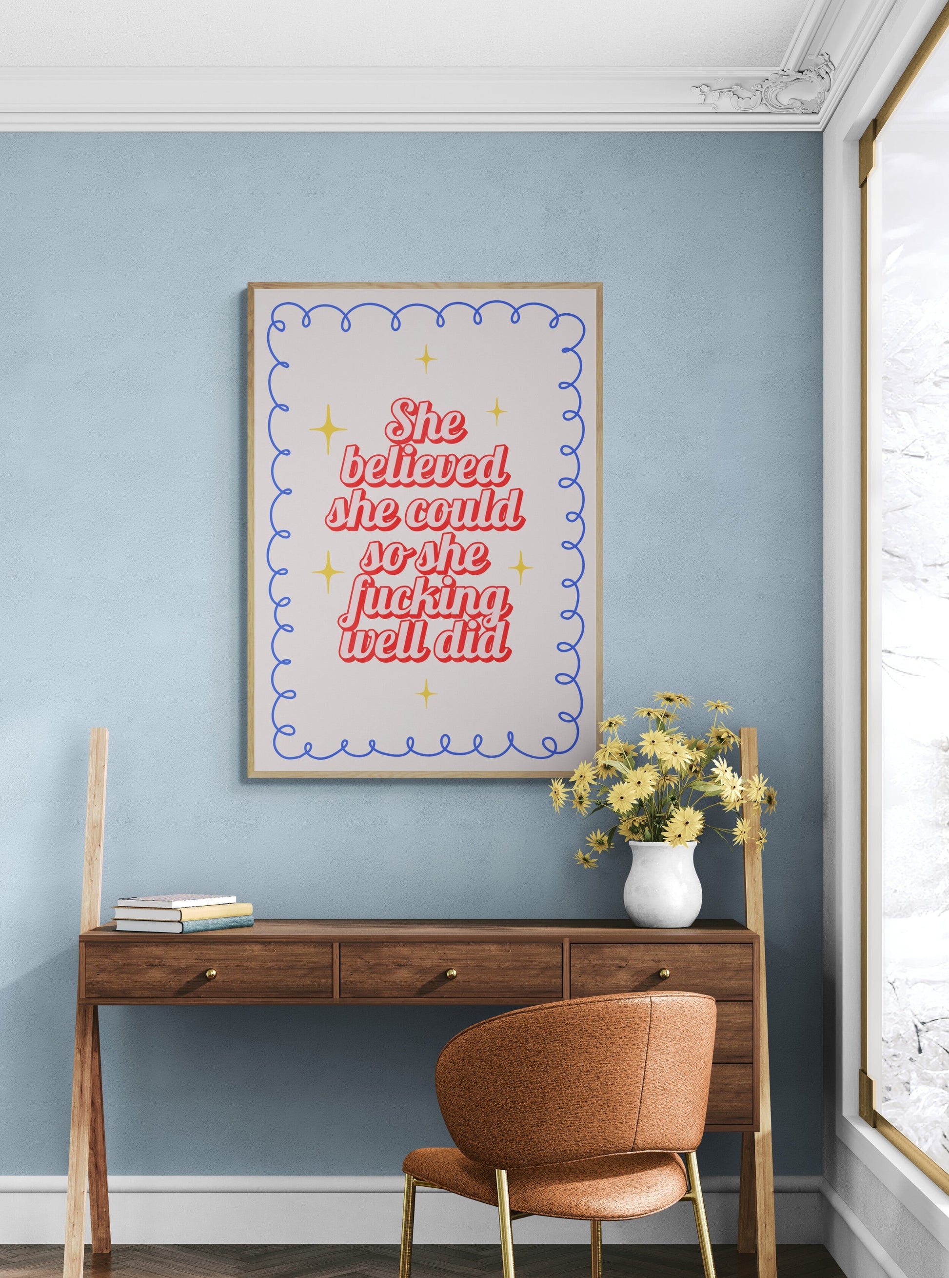 Wooden desk with a chair against a blue wall with a motivational poster saying "she believed she would so she fucking well did".