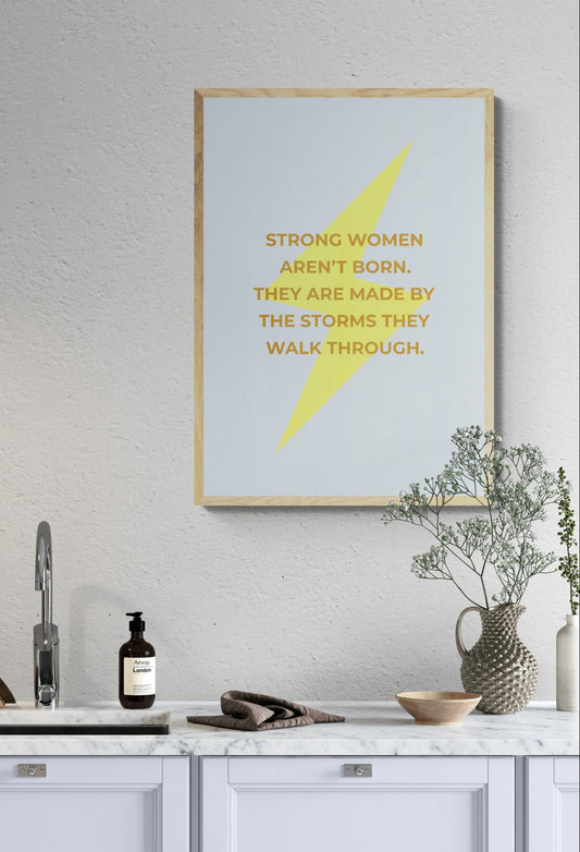 Kitchen interior with motivational poster on the wall. Strong women aren't born. They are made by the storms they walk through wording on top of a lightening bolt on a pale blue background. 