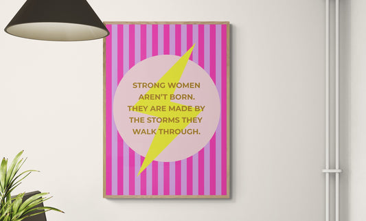 Motivational poster on a wall above a desk with office furniture saying Strong women aren't born. They are made by the storms they walk through on top of a lightening bolt.
