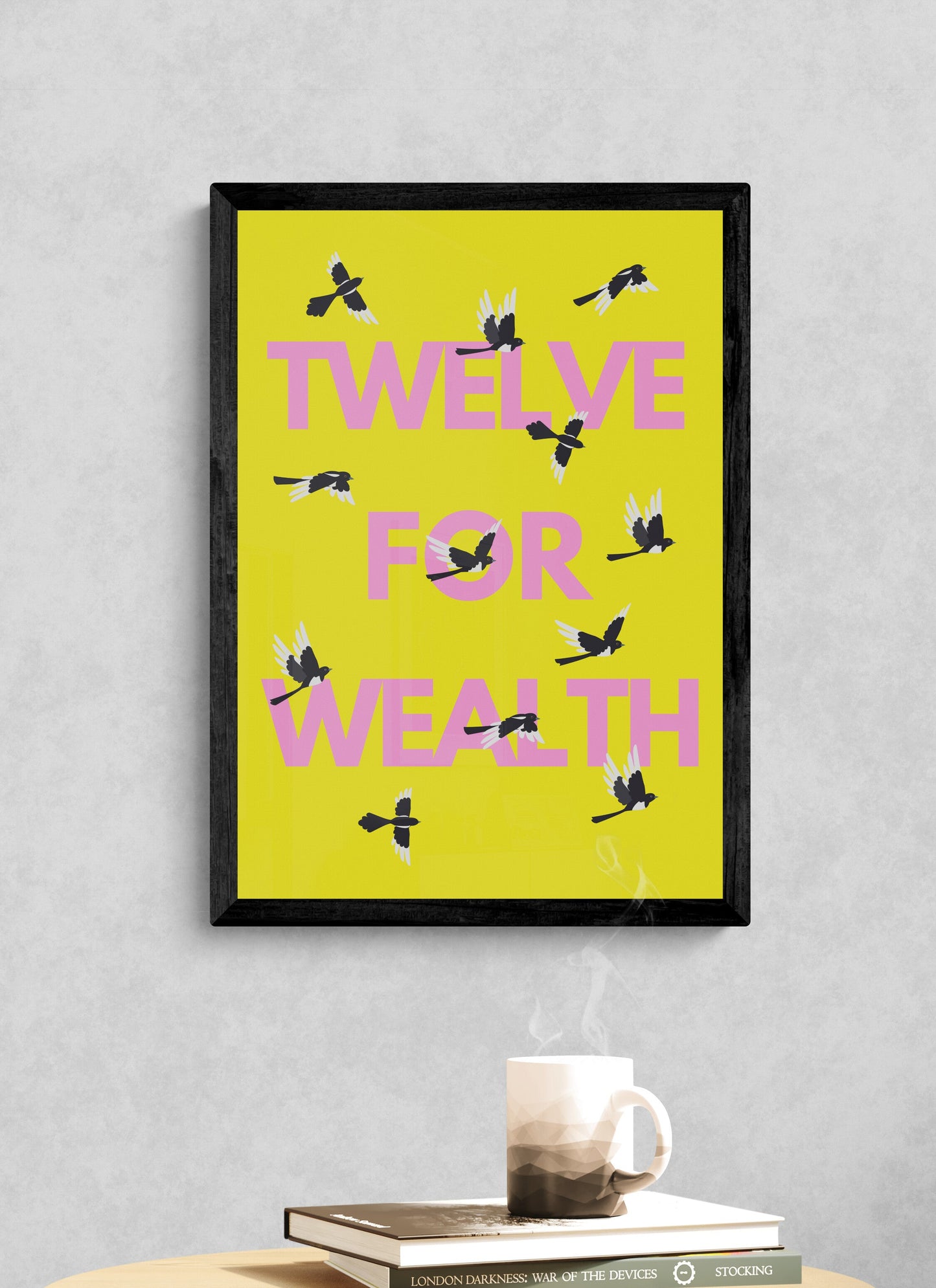Framed artwork with 'Twelve for Wealth' text and twelve magpies positioned on a yellow background, placed on a table against a gray wall.