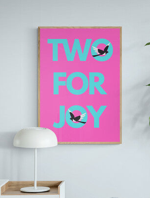 Living room with a pink poster reading 'TWO FOR JOY' with two magpies signifying luck from seeing two together and a plant.