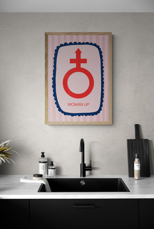 Art print featuring "woman up" wording below the female symbol placed in a border. As a play on "man up". Art print hung above a sink. 