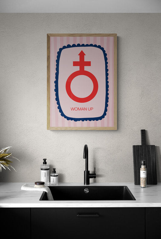 Art print featuring "woman up" wording below the female symbol placed in a border. As a play on "man up". Art print hung above a sink. 