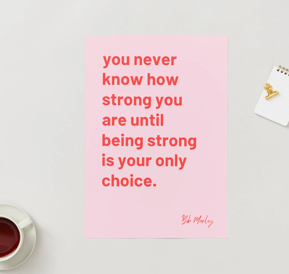Motivational poster with a quote on a pink background, placed on a surface with a cup of tea.